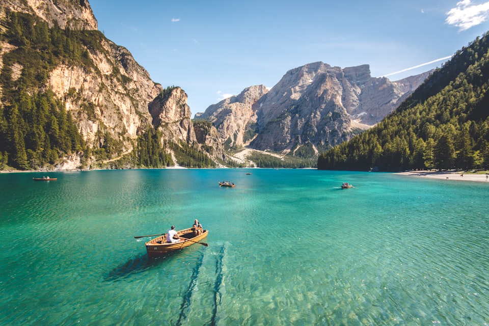 Turquoise lake below a forest and mountain peaks